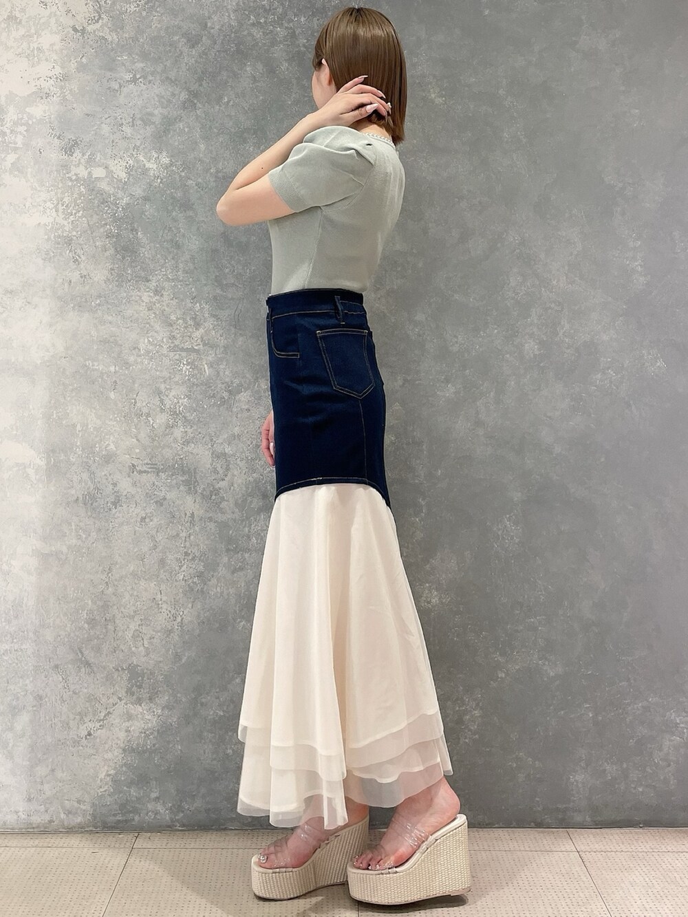 グリーン系のニット/セーター、ブルー系のスカート、ホワイト系のサンダルを着用したレディースの春コーディネートの2枚目の写真