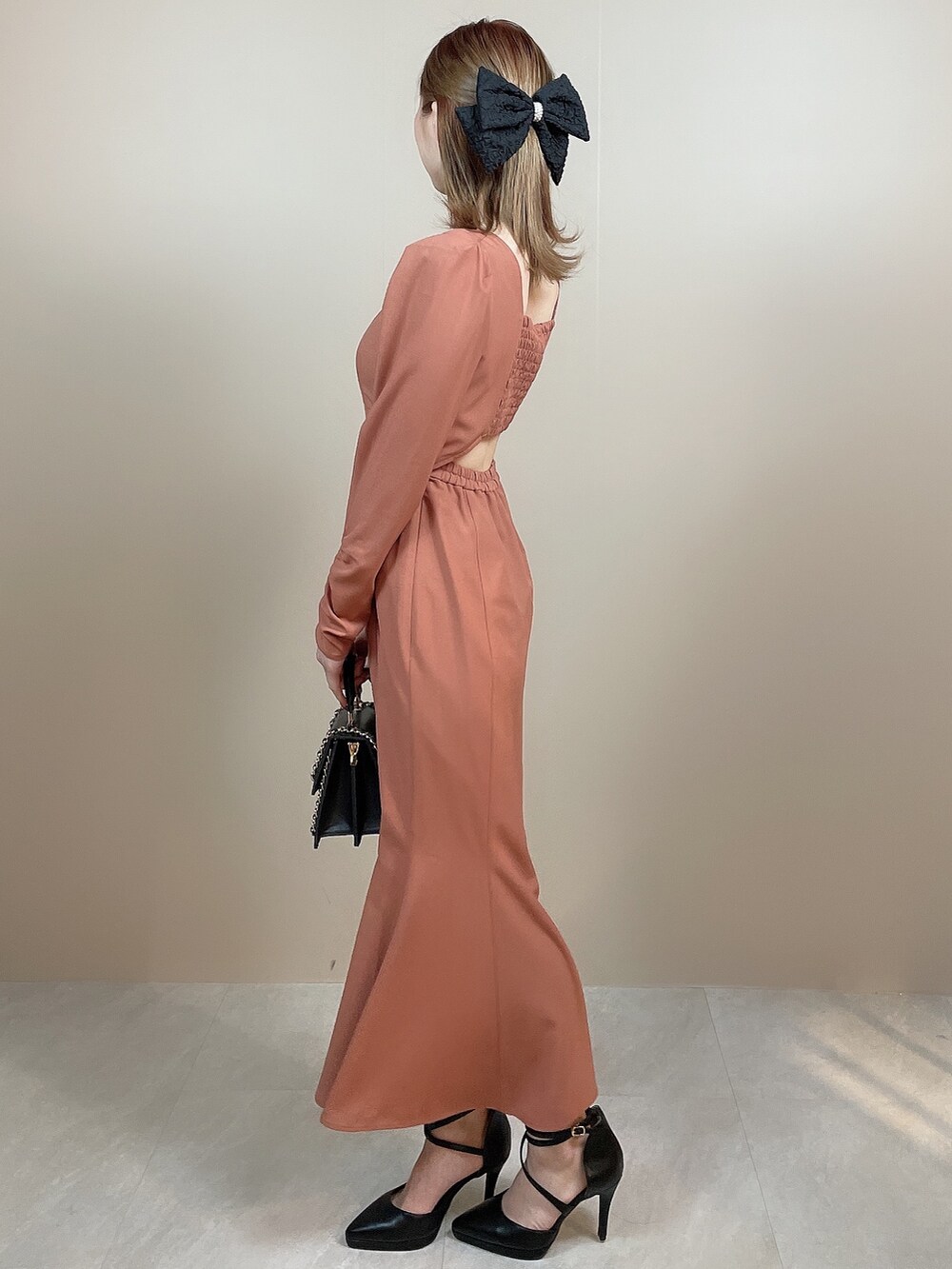 ブラック系のハンドバッグ、オレンジ系のワンピース、ブラック系のパンプスを着用したレディースの冬コーディネートの3枚目の写真