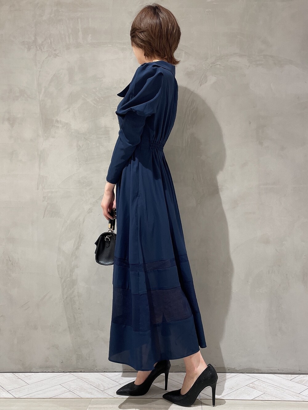 ブラック系のハンドバッグ、ブルー系のワンピース、ブラック系のパンプスを着用したレディースの冬コーディネートの3枚目の写真