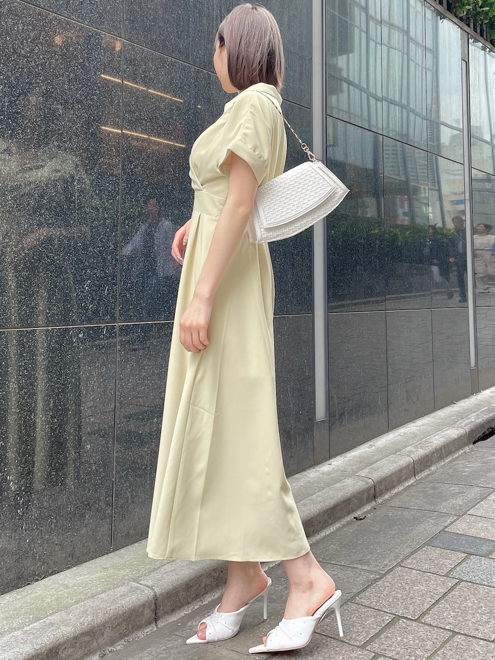 イエロー系のワンピース、ホワイト系のサンダル、ホワイト系のハンドバッグを着用したレディースの春コーディネートの3枚目の写真