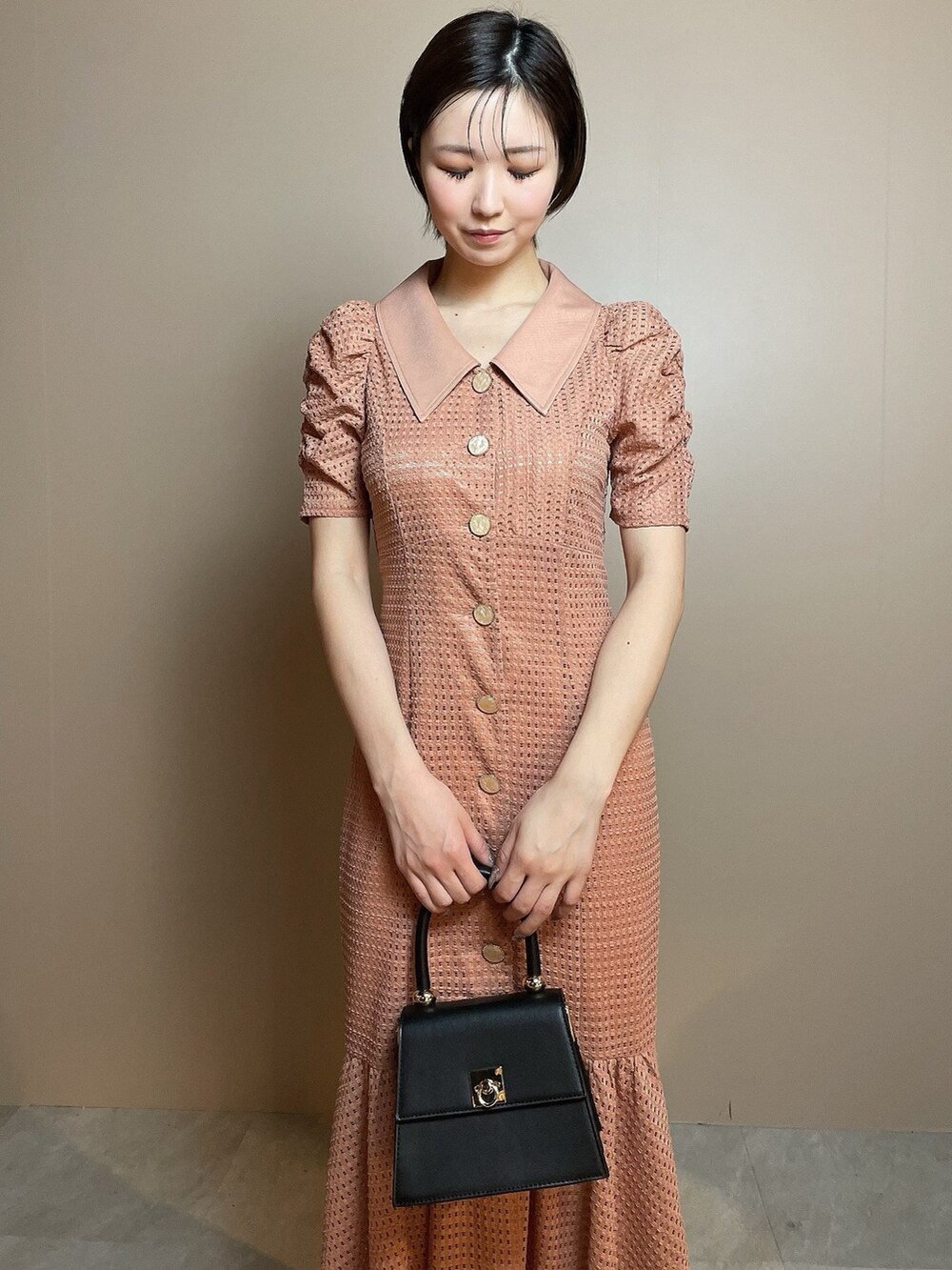 オレンジ系のワンピース、ブラック系のハンドバッグ、ブラック系のパンプスを着用したレディースの冬コーディネートの6枚目の写真