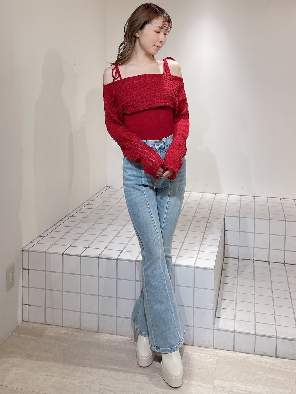 レッド系のニット/セーター、ブルー系のデニムパンツ、ホワイト系のブーツを着用したレディースの冬コーディネートの2枚目の写真