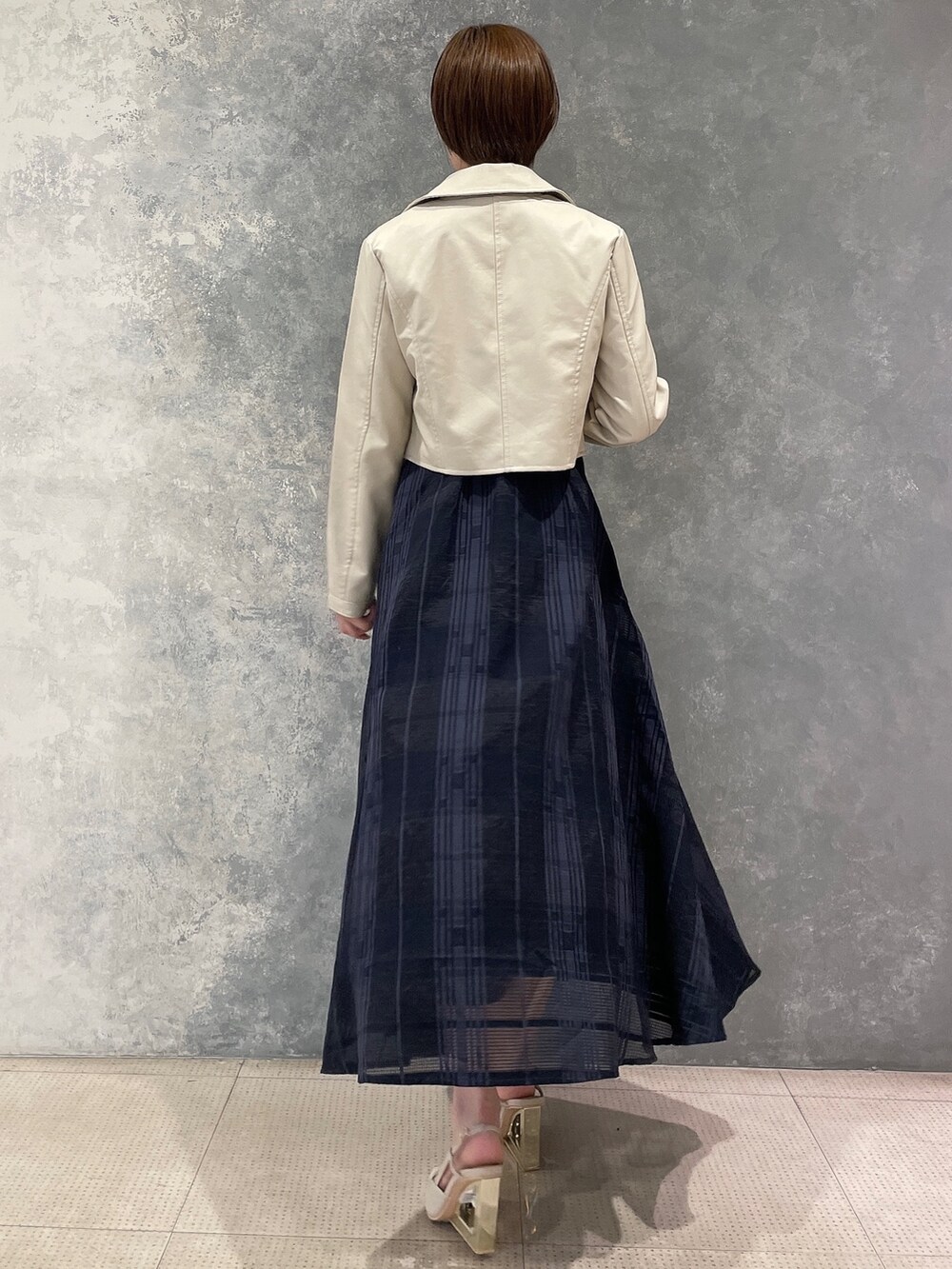 ホワイト系のライダースジャケット、ベージュ系のサンダル、ブルー系のワンピースを着用したレディースの夏コーディネートの2枚目の写真