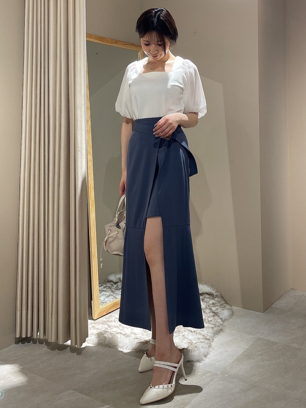 ホワイト系のハンドバッグ、ホワイト系のパンプス、ブルー系のスカートを着用したレディースの春コーディネートの2枚目の写真