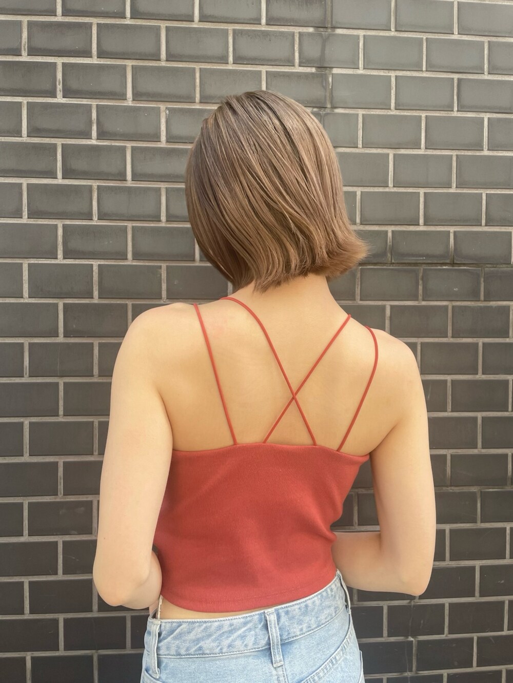 オレンジ系のキャミソール、ブルー系のデニムパンツ、ホワイト系のサンダルを着用したレディースの春コーディネートの5枚目の写真