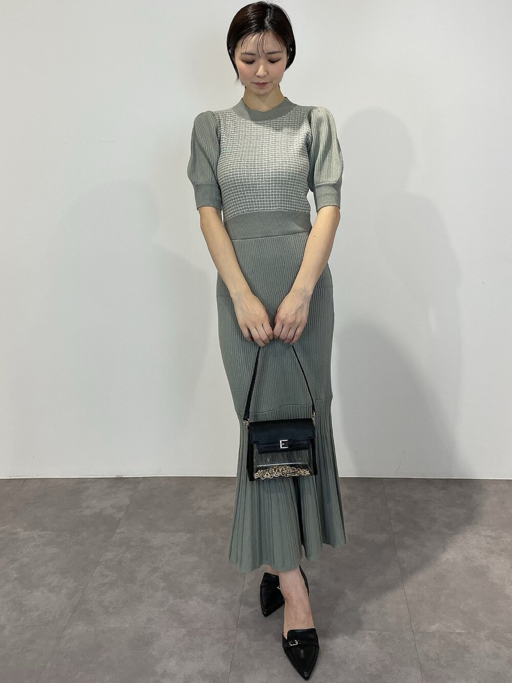 グリーン系のワンピース、ブラック系のパンプス、ブラック系のハンドバッグを着用したレディースの冬コーディネートの2枚目の写真