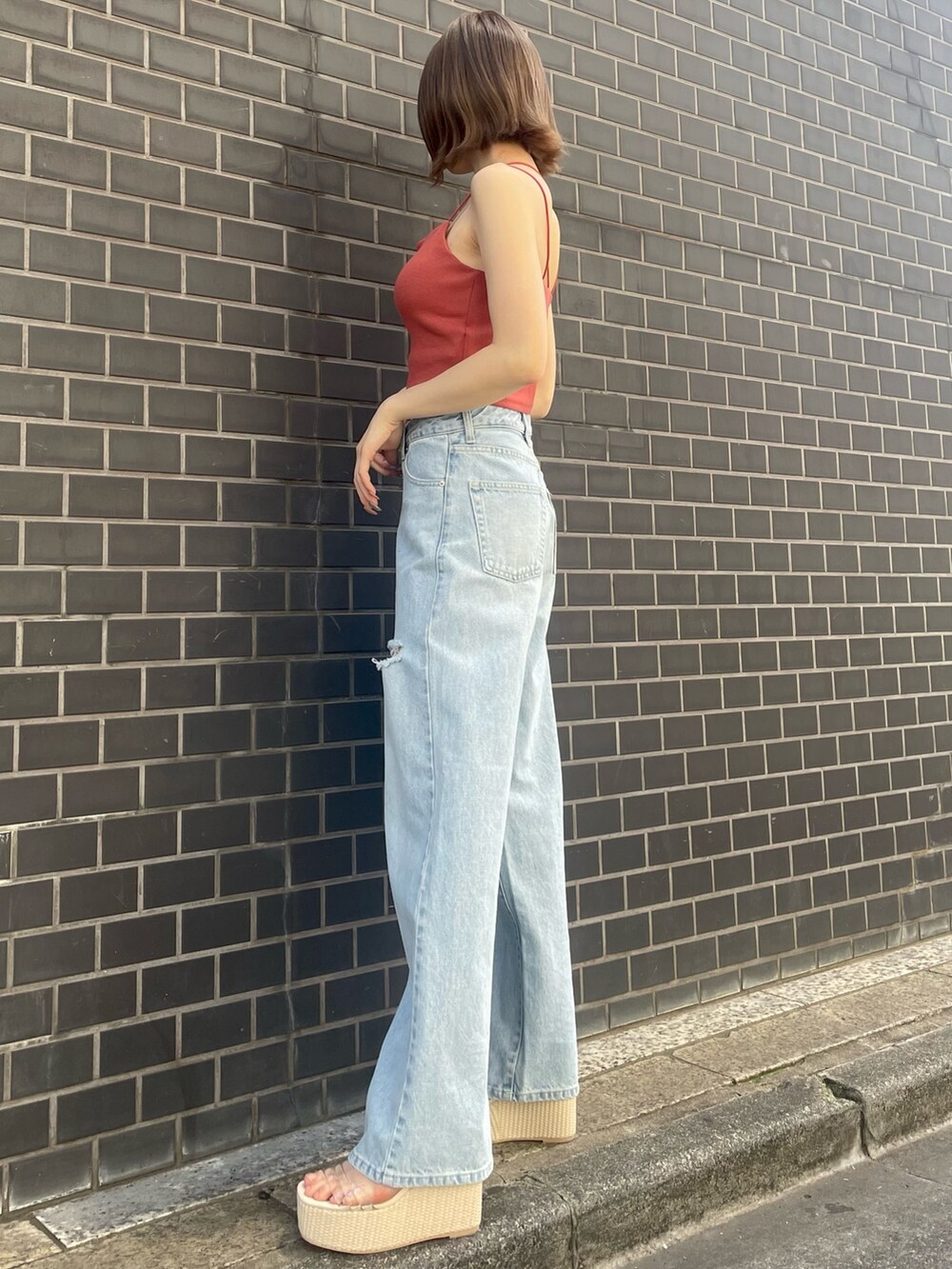 オレンジ系のキャミソール、ブルー系のデニムパンツ、ホワイト系のサンダルを着用したレディースの春コーディネートの4枚目の写真