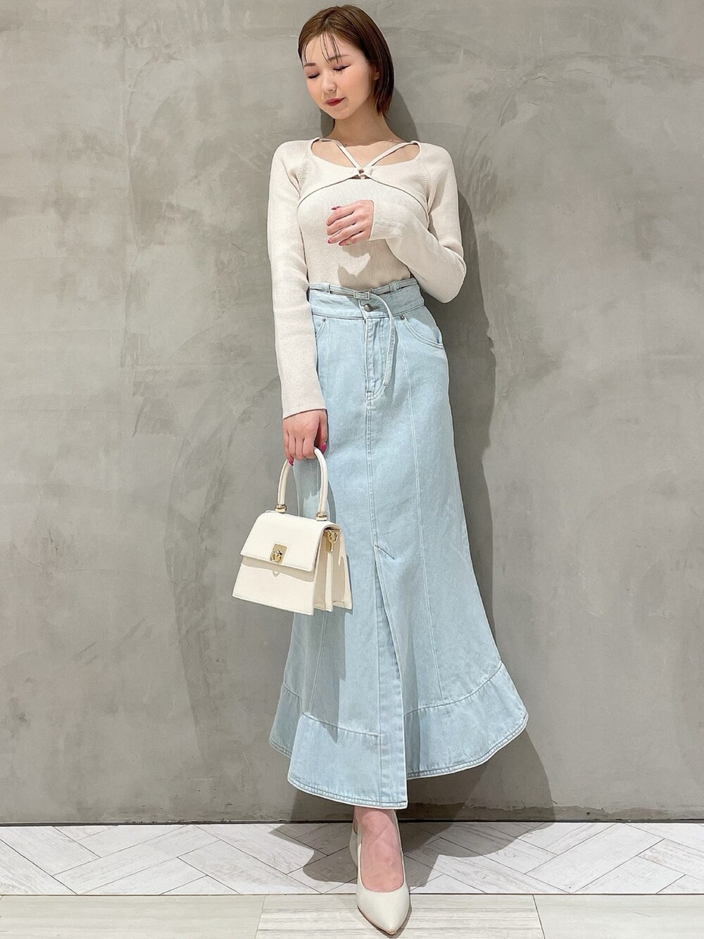 ホワイト系のハンドバッグ、ホワイト系のパンプス、ブルー系のデニムスカートを着用したレディースの冬コーディネートの7枚目の写真