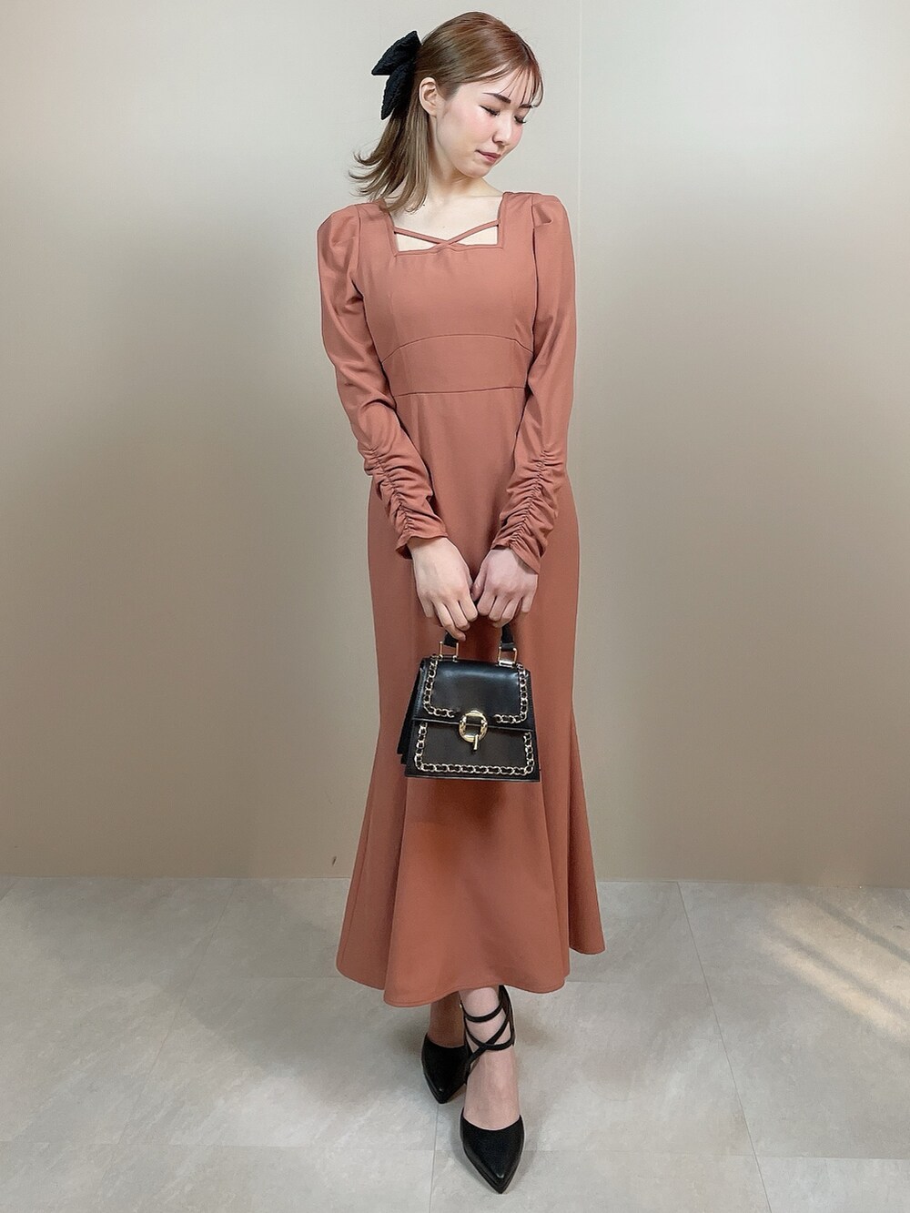 ブラック系のハンドバッグ、オレンジ系のワンピース、ブラック系のパンプスを着用したレディースの冬コーディネートの2枚目の写真