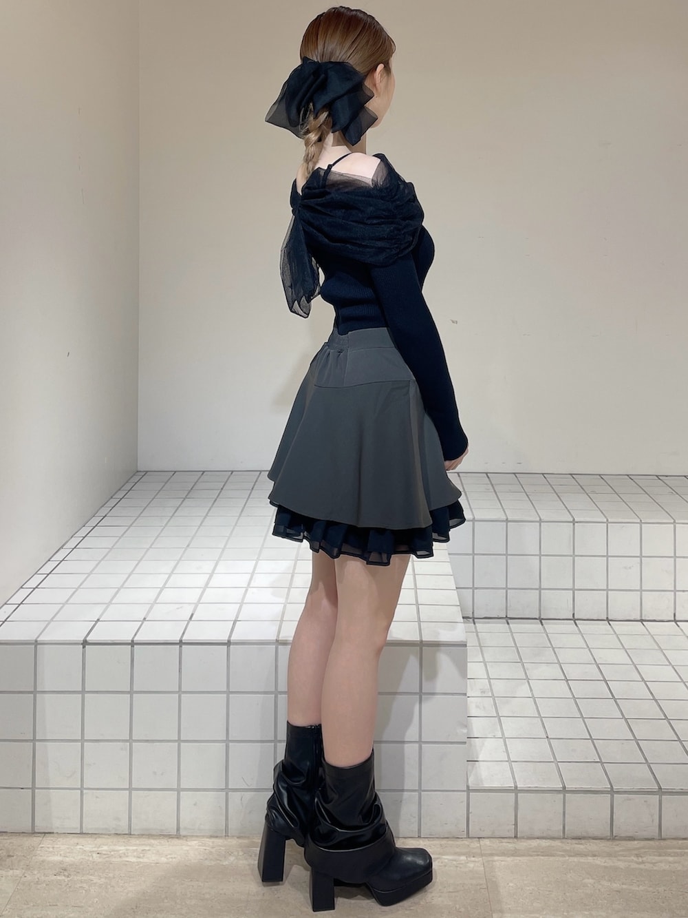 グレー系のスカート、ブラック系のニット/セーター、ブラック系のブーツを着用したレディースの春コーディネートの2枚目の写真