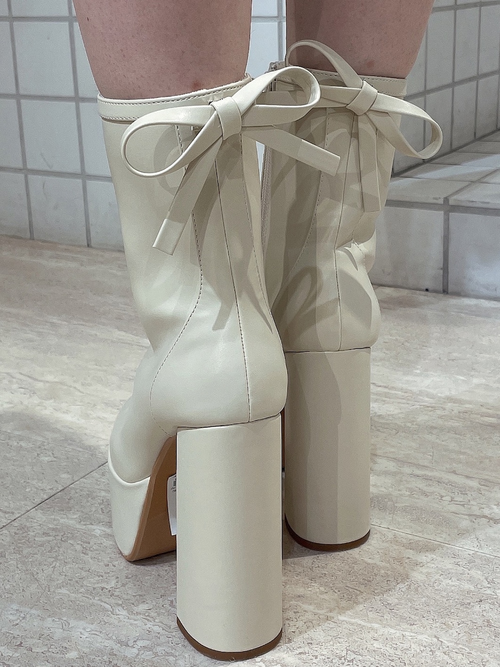 ホワイト系のハンドバッグ、ホワイト系のブーツ、ブラック系のワンピースを着用したレディースの冬コーディネートの8枚目の写真