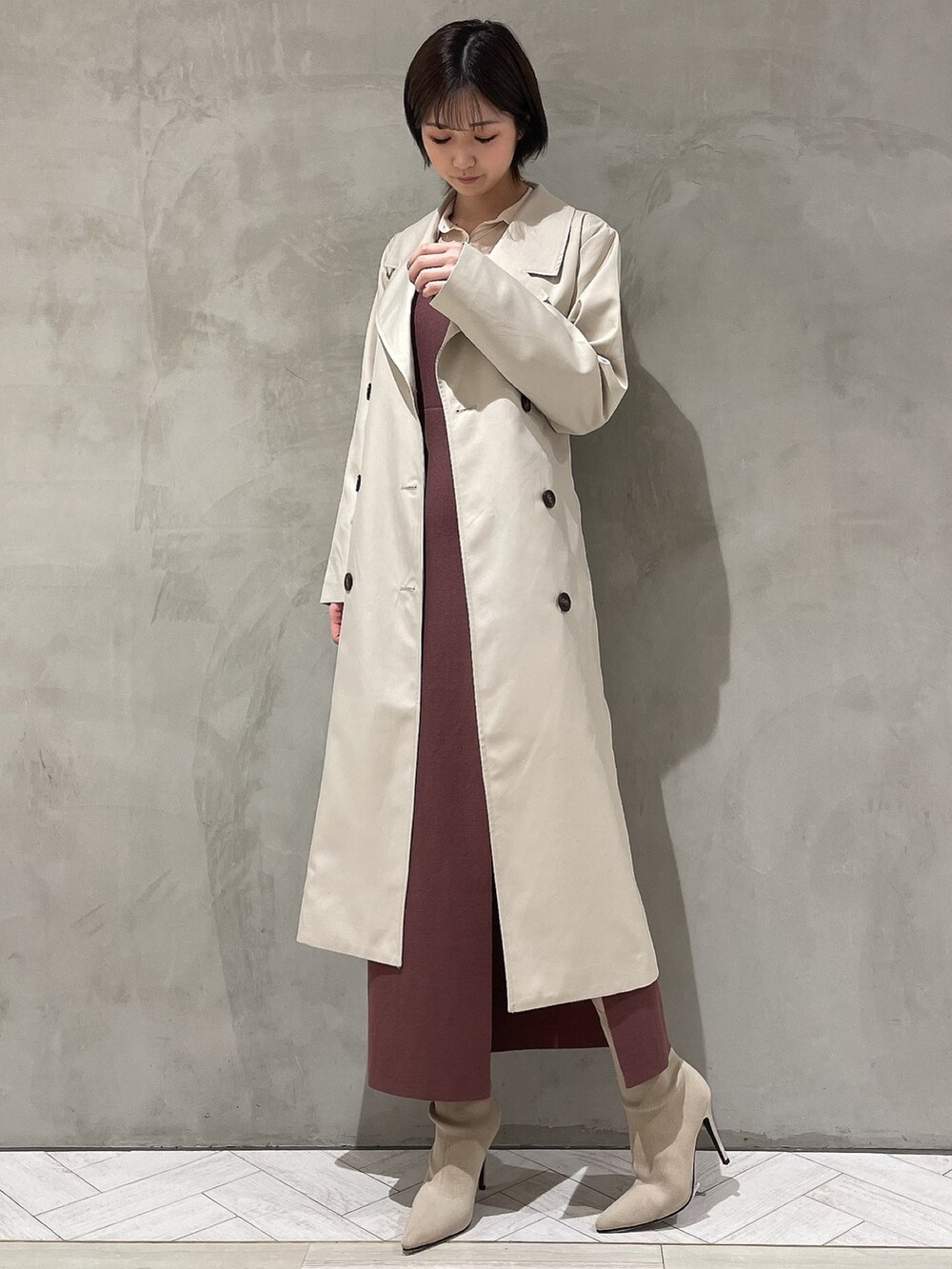 ベージュ系のトレンチコート、ブラウン系のワンピース、ホワイト系のブーツを着用したレディースの冬コーディネートの2枚目の写真