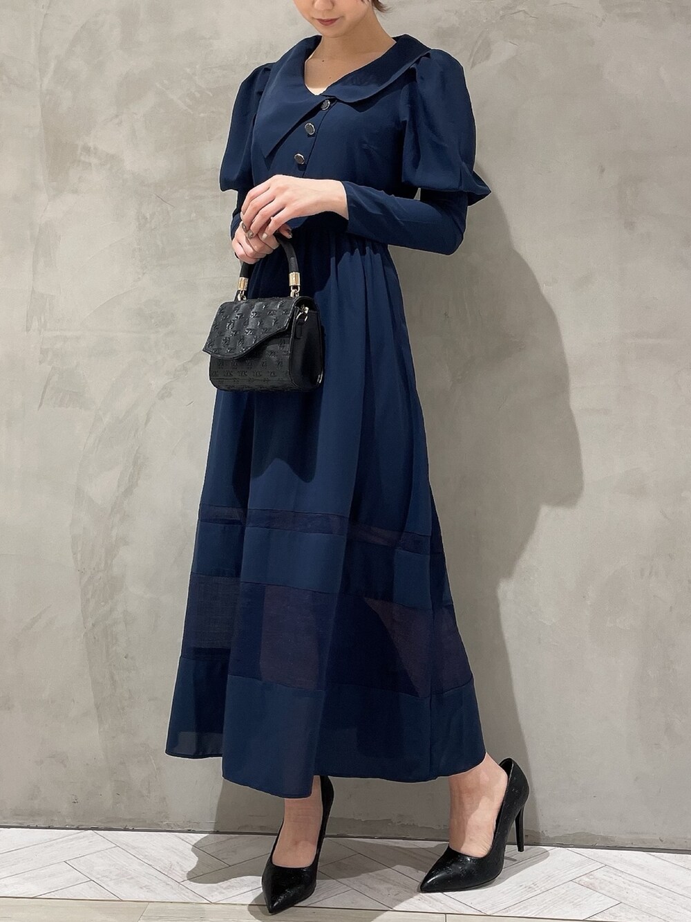 ブラック系のハンドバッグ、ブルー系のワンピース、ブラック系のパンプスを着用したレディースの冬コーディネートの2枚目の写真