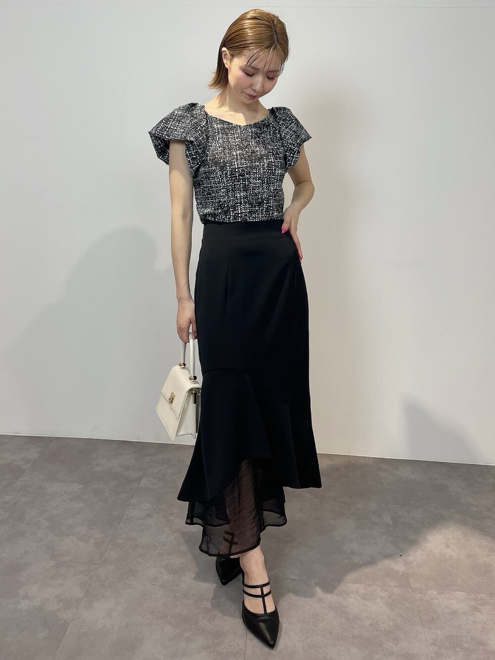 ブラック系のシャツ/ブラウス、ホワイト系のハンドバッグ、ブラック系のパンプスを着用したレディースの春コーディネートの2枚目の写真