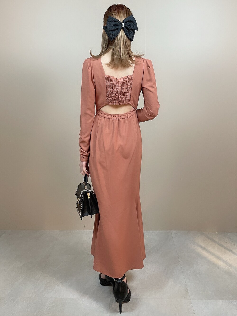 ブラック系のハンドバッグ、オレンジ系のワンピース、ブラック系のパンプスを着用したレディースの冬コーディネートの4枚目の写真