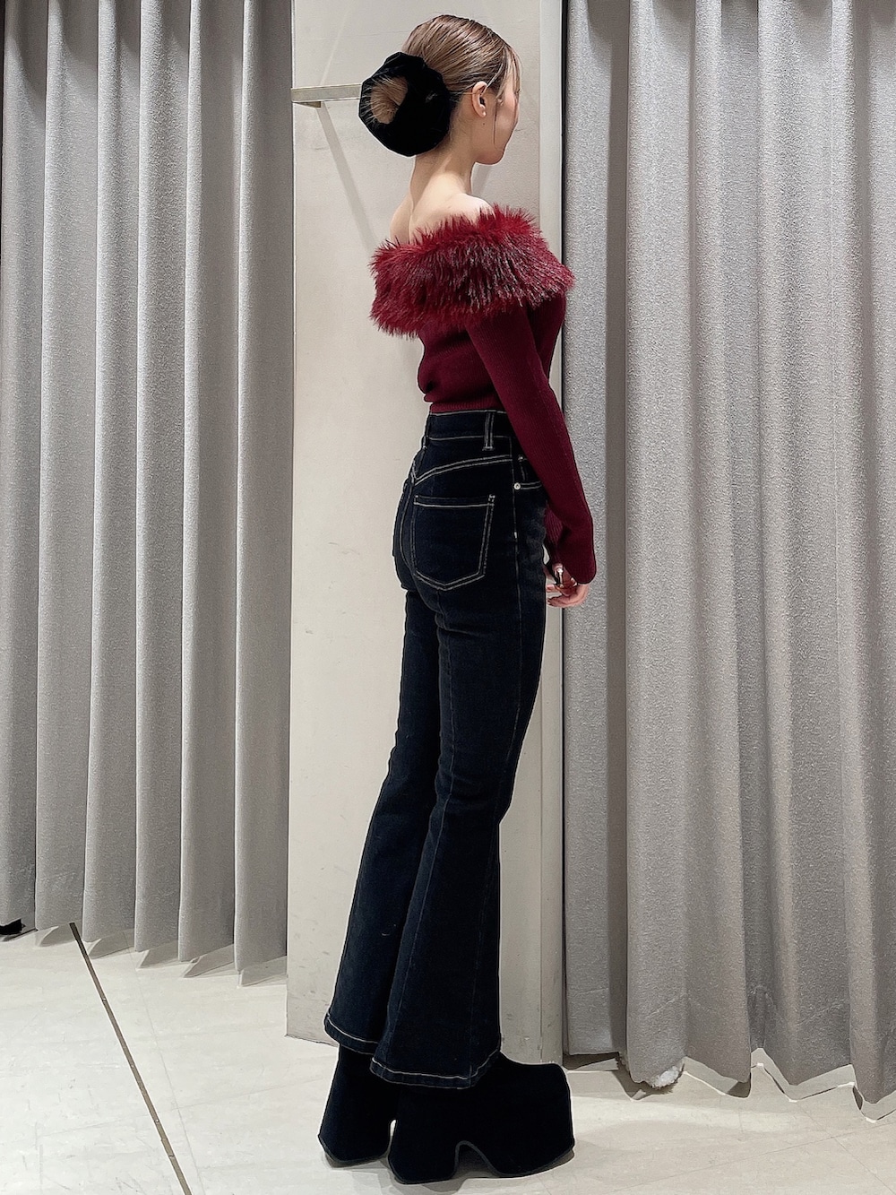 レッド系のニット/セーター、ブラック系のデニムパンツ、ブラック系のブーツを着用したレディースの秋コーディネートの2枚目の写真
