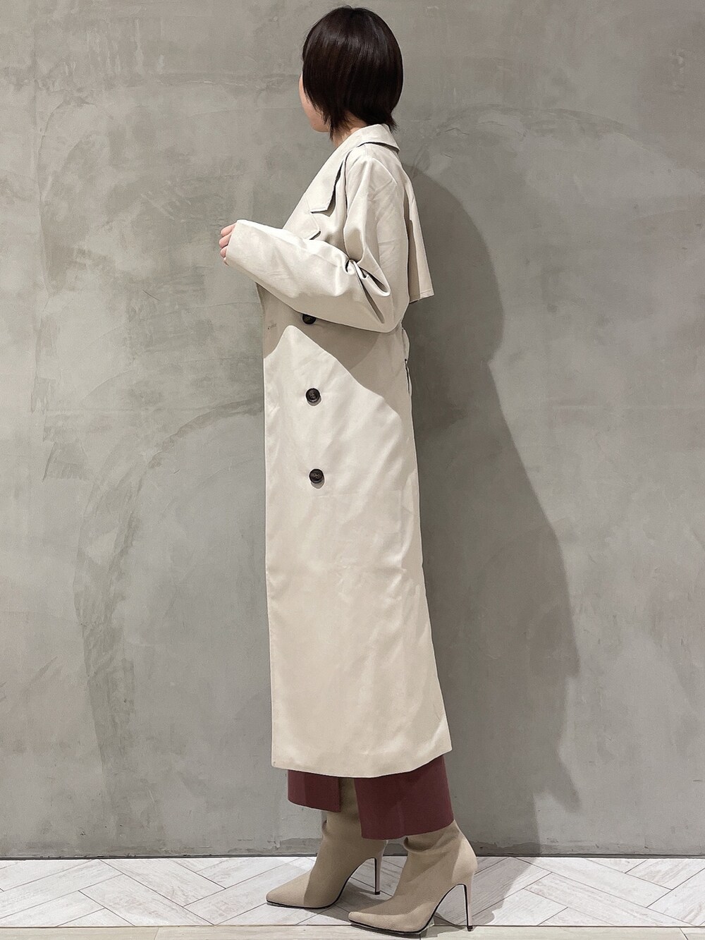 ベージュ系のトレンチコート、ブラウン系のワンピース、ホワイト系のブーツを着用したレディースの冬コーディネートの3枚目の写真