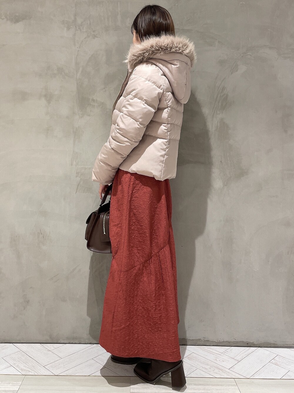 ベージュ系のダウンジャケット/コート、ブラック系のニット/セーター、ブラウン系のハンドバッグを着用したレディースの秋コーディネートの2枚目の写真