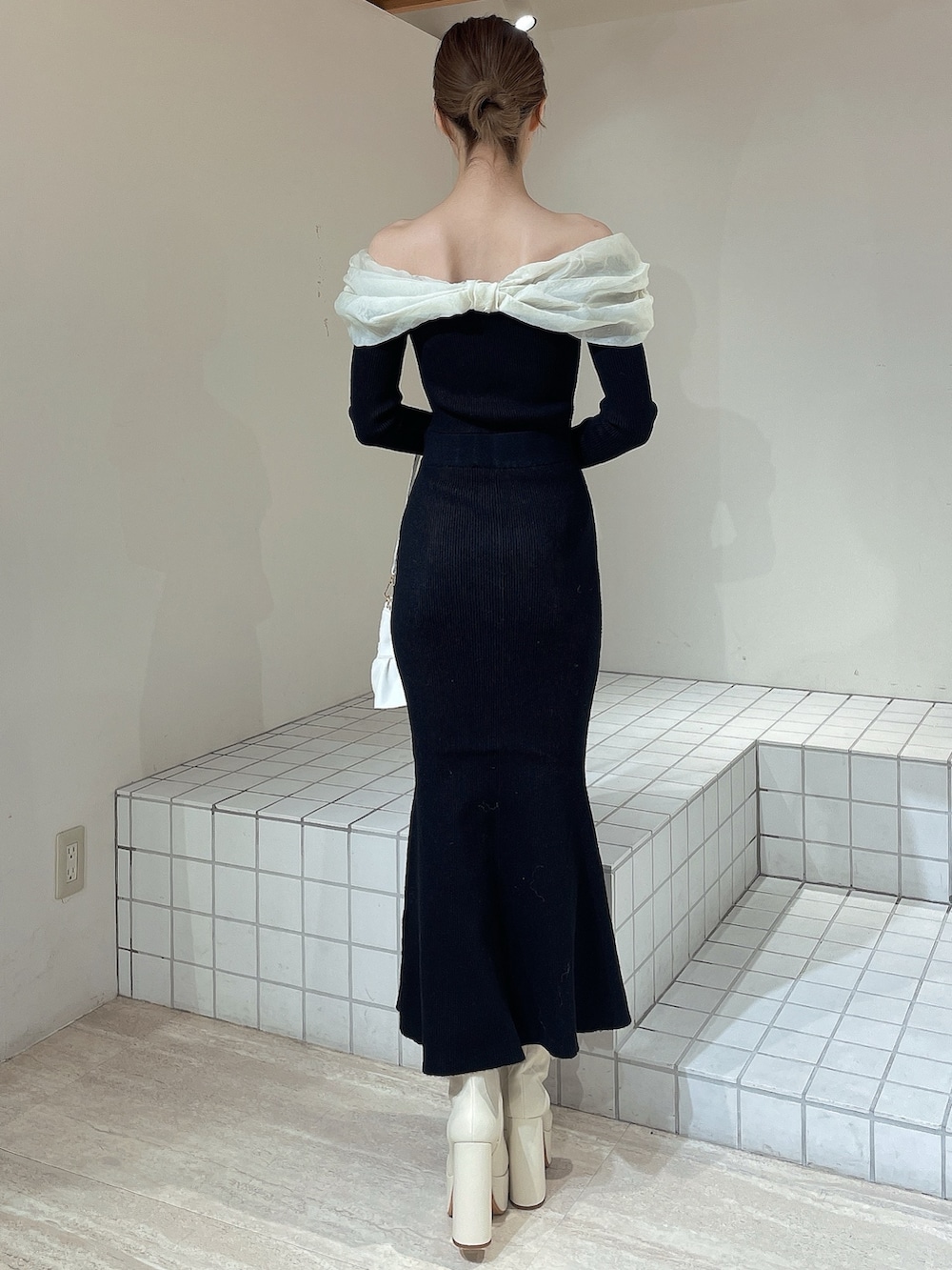 ホワイト系のハンドバッグ、ホワイト系のブーツ、ブラック系のワンピースを着用したレディースの冬コーディネートの4枚目の写真