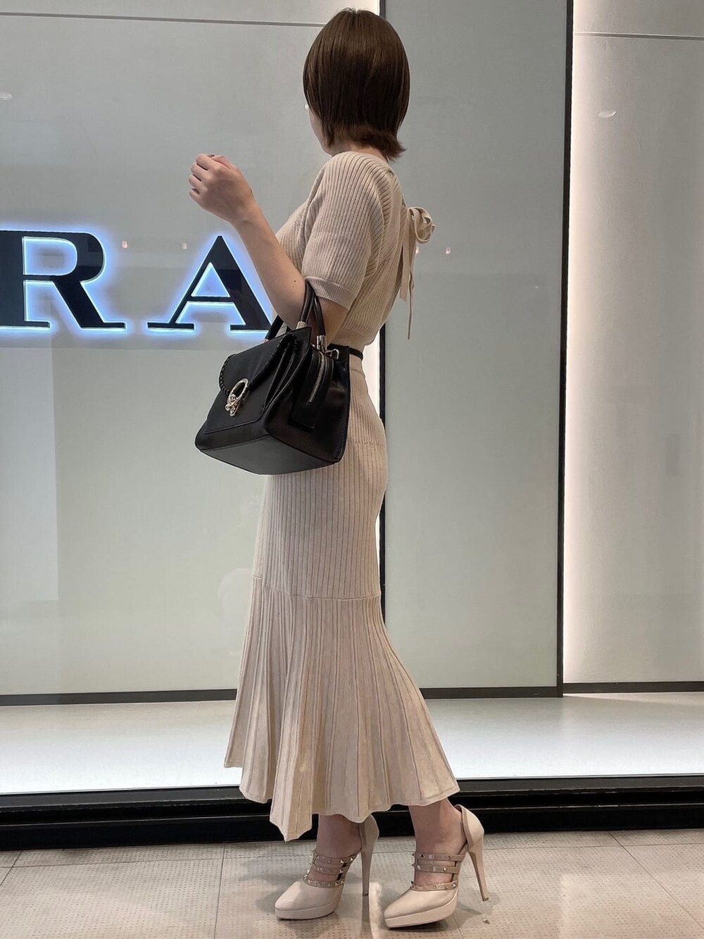 ブラック系のハンドバッグ、ベージュ系のワンピース、ベージュ系のパンプスを着用したレディースの秋コーディネートの3枚目の写真