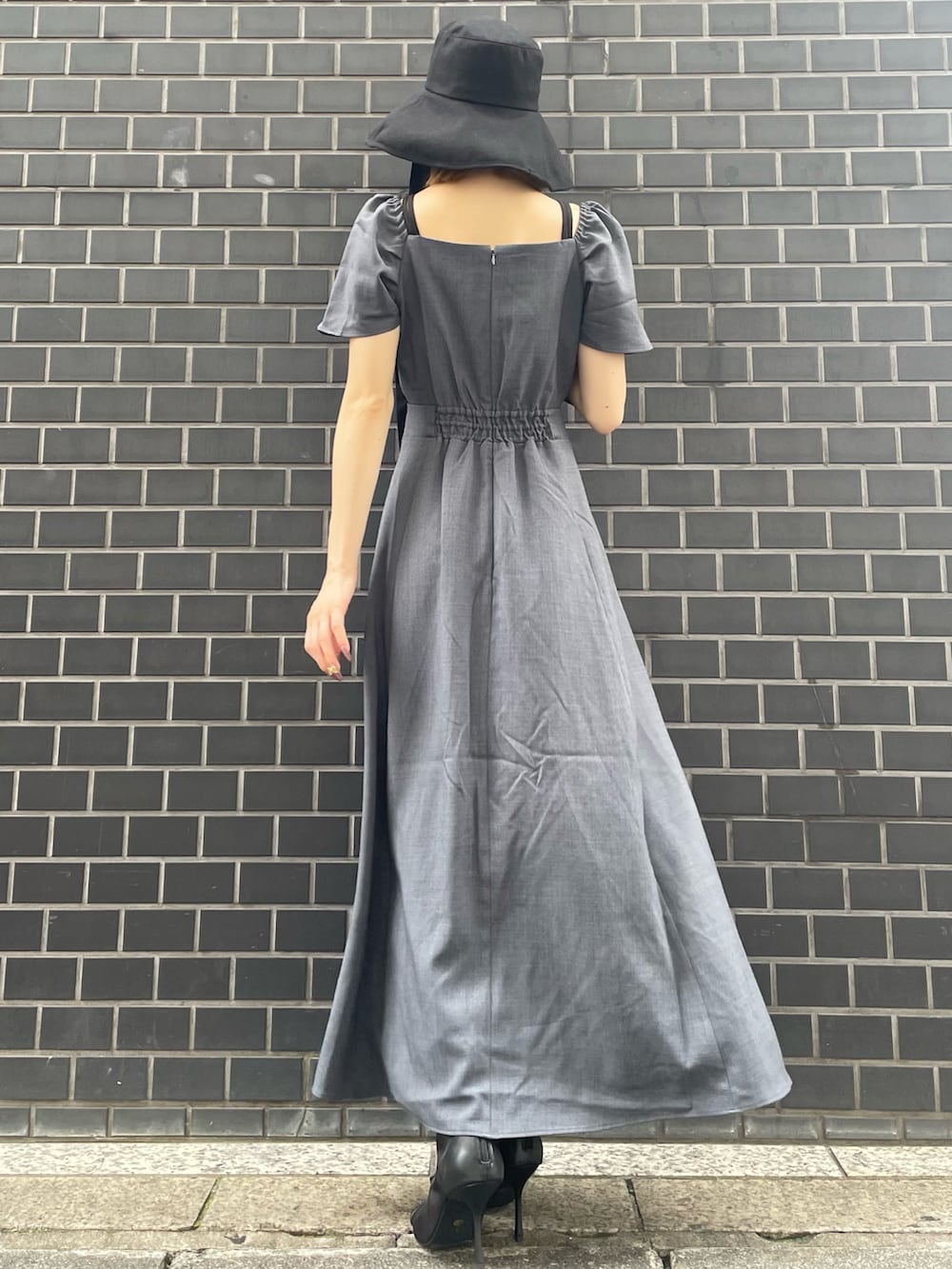 グレー系のワンピース、ブラック系のブーツ、ブラック系のハットを着用したレディースの夏コーディネートの2枚目の写真