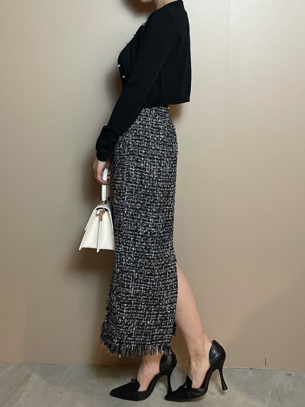 ホワイト系のハンドバッグ、ブラック系のカーディガン/ボレロ、ブラック系のスカートを着用したレディースの冬コーディネートの3枚目の写真