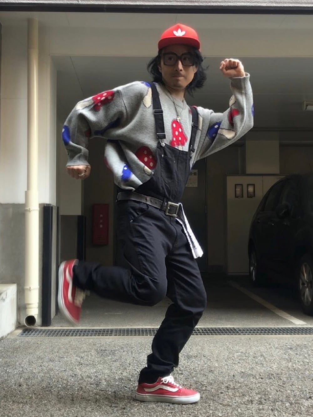 レッド系のスニーカー、ブラック系のサロペット/オーバーオール、レッド系のキャップを着用したメンズの春コーディネートの2枚目の写真