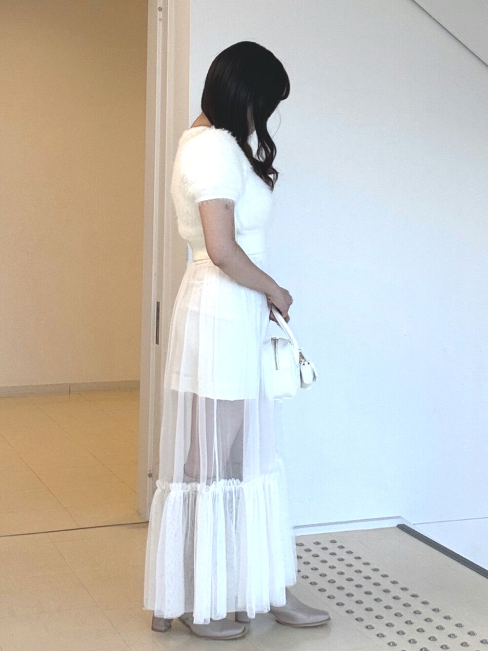 ホワイト系のニット/セーター、ホワイト系のスカート、ベージュ系のブーツを着用したレディースの夏コーディネートの2枚目の写真