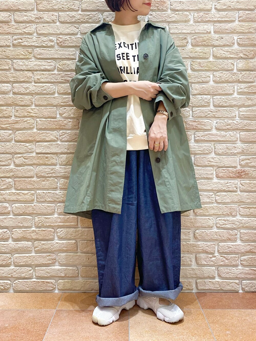 ホワイト系のTシャツ/カットソー、グリーン系のステンカラーコート、ブルー系のデニムパンツを着用したレディースの春コーディネートの2枚目の写真