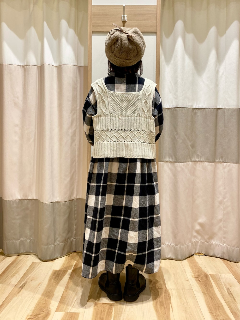 ブラック系のワンピース、ホワイト系のベスト、ブラック系のブーツを着用したレディースの冬コーディネートの3枚目の写真