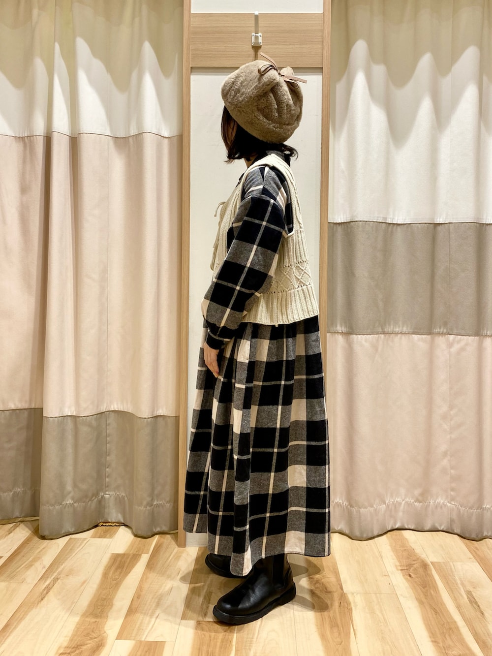 ブラック系のワンピース、ホワイト系のベスト、ブラック系のブーツを着用したレディースの冬コーディネートの2枚目の写真