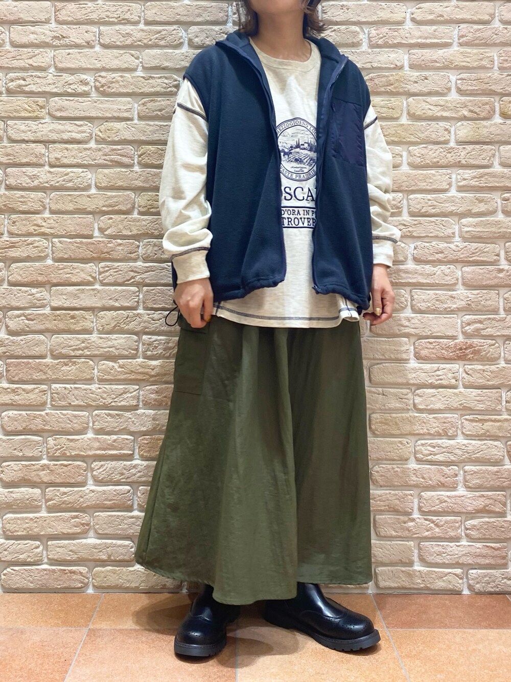 グレー系のTシャツ/カットソー、ブルー系のベスト、グリーン系のスカートを着用したレディースの秋コーディネートの2枚目の写真