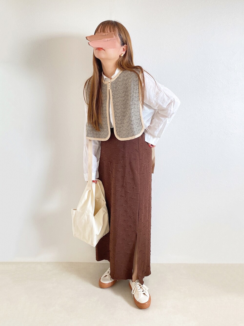 ベージュ系のベスト、ブラウン系のスカート、ホワイト系のトートバッグを着用したレディースの秋コーディネートの2枚目の写真