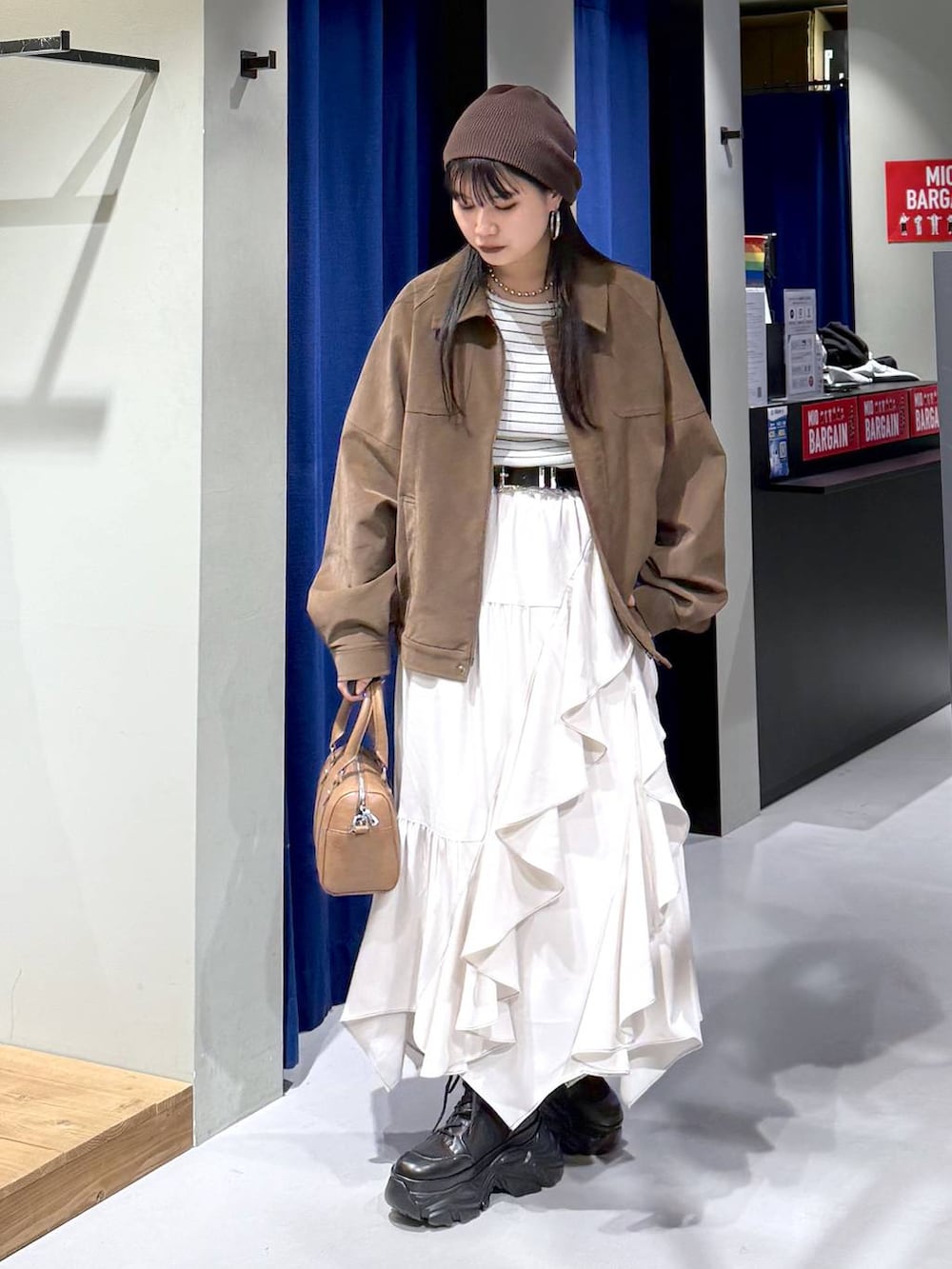 ブラック系のブーツ、ベージュ系のスカート、ブラウン系のボストンバッグを着用したレディースの春コーディネートの2枚目の写真