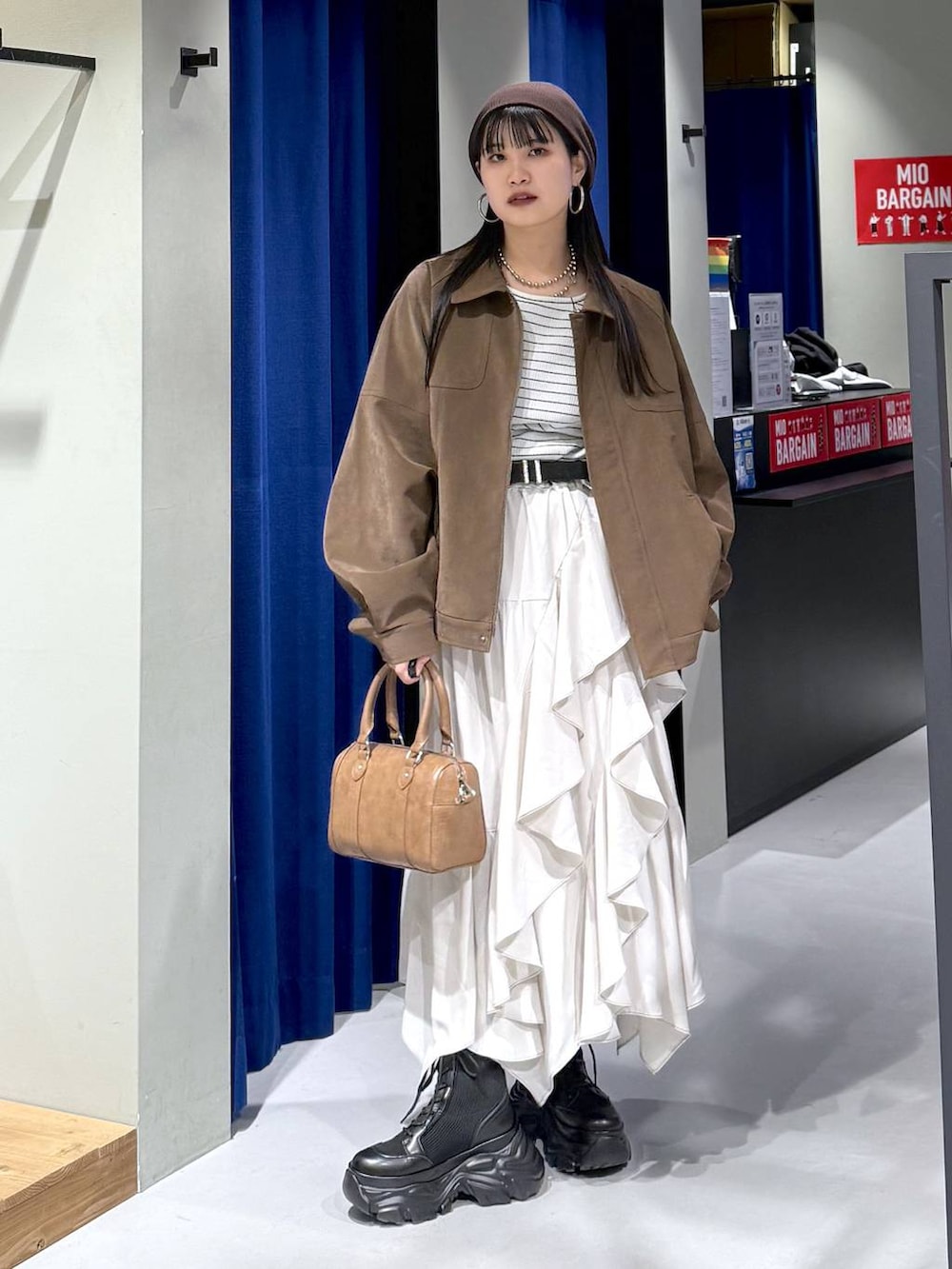 ブラック系のブーツ、ベージュ系のスカート、ブラウン系のボストンバッグを着用したレディースの春コーディネートの3枚目の写真