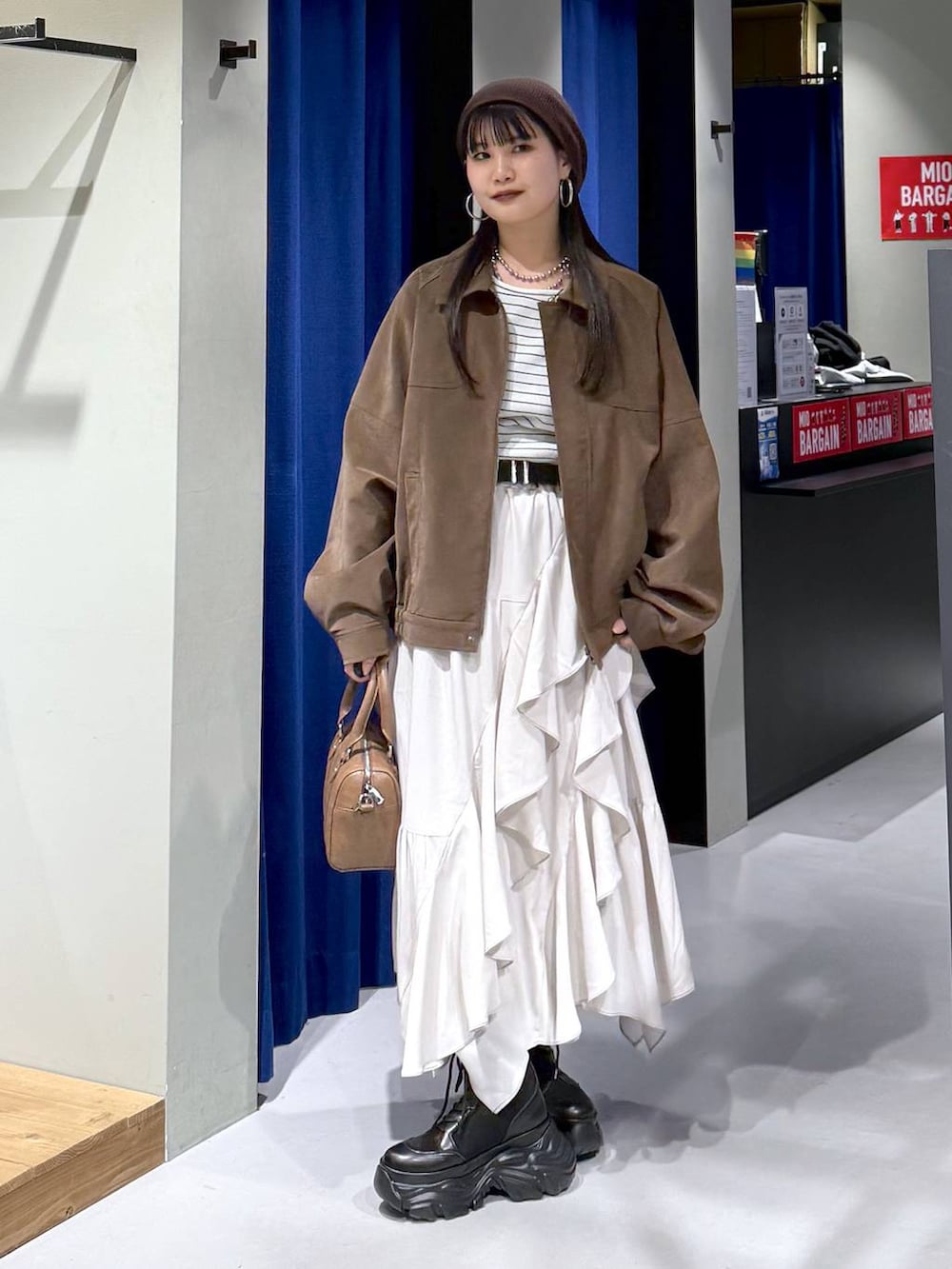 ブラック系のブーツ、ベージュ系のスカート、ブラウン系のボストンバッグを着用したレディースの春コーディネートの7枚目の写真