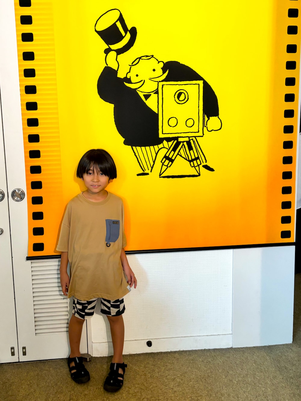ブラック系のその他パンツ、ブラック系のサンダル、ベージュ系のTシャツ/カットソーを着用したキッズの夏コーディネートの2枚目の写真
