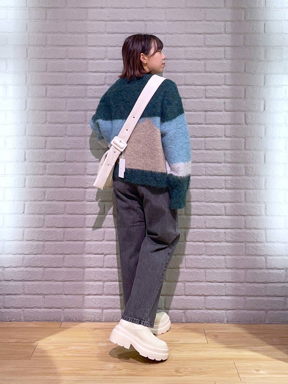 ブラック系のデニムパンツ、ホワイト系のブーツ、ホワイト系のショルダーバッグを着用したレディースの秋コーディネートの3枚目の写真