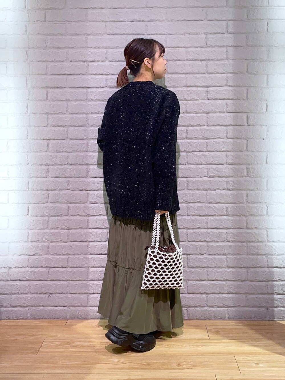 ホワイト系のショルダーバッグ、ブラック系のニット/セーター、ブラック系のスニーカーを着用したレディースの秋コーディネートの3枚目の写真