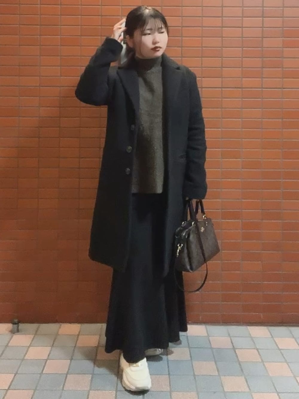 ブラウン系のショルダーバッグ、ブラウン系のニット/セーター、ブラック系のスカートを着用したレディースの秋コーディネートの2枚目の写真