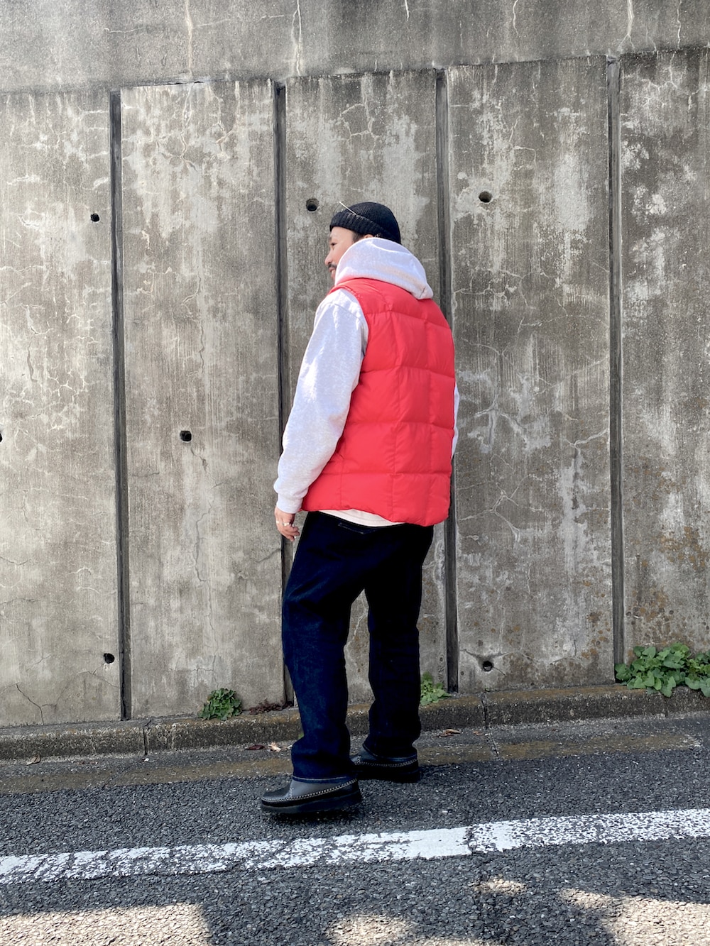 ブラック系のブーツ、ブルー系のデニムパンツ、レッド系のダウンベストを着用したメンズの春コーディネートの2枚目の写真