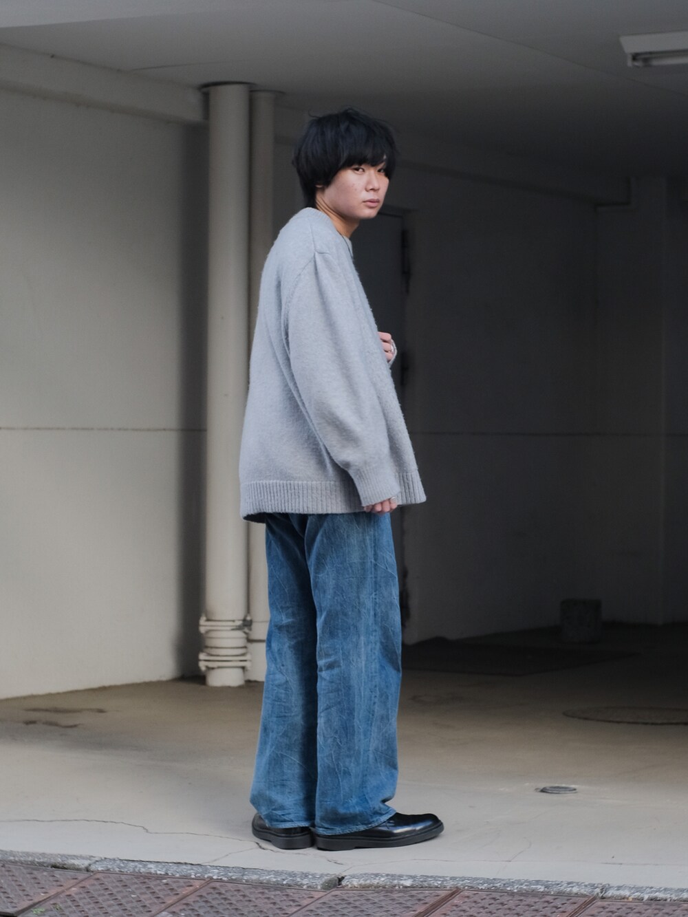 グレー系のニット/セーター、ブルー系のデニムパンツ、ブラック系のドレスシューズを着用したメンズの冬コーディネートの5枚目の写真