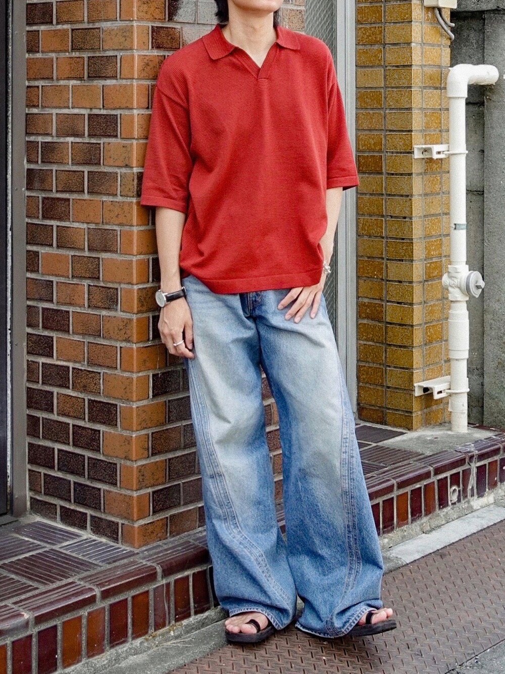 レッド系のポロシャツ、ブラック系のサンダル、ブルー系のデニムパンツを着用したメンズの夏コーディネートの3枚目の写真
