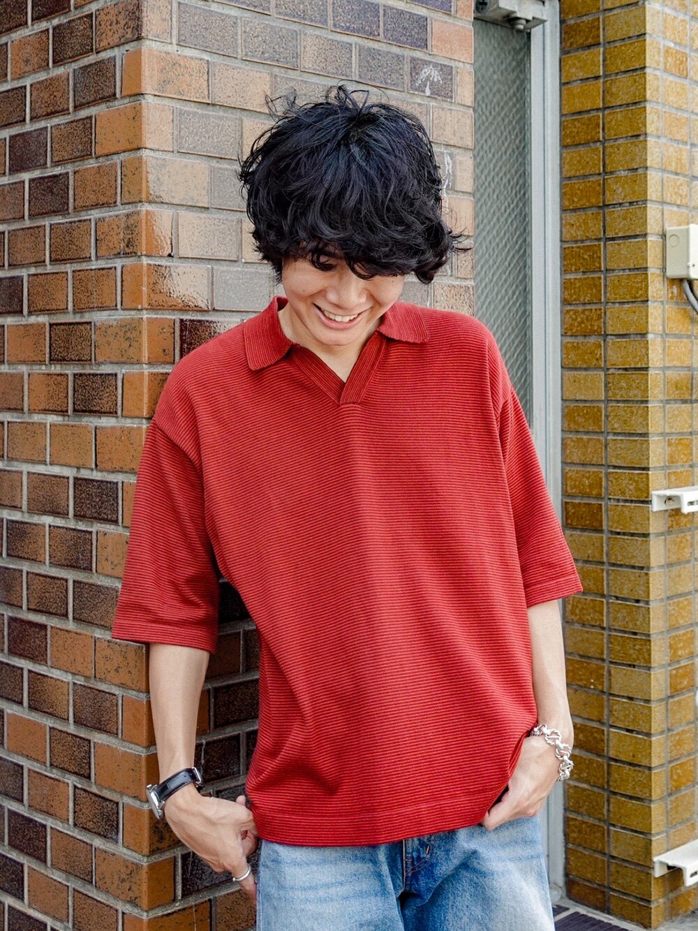 レッド系のポロシャツ、ブラック系のサンダル、ブルー系のデニムパンツを着用したメンズの夏コーディネートの2枚目の写真