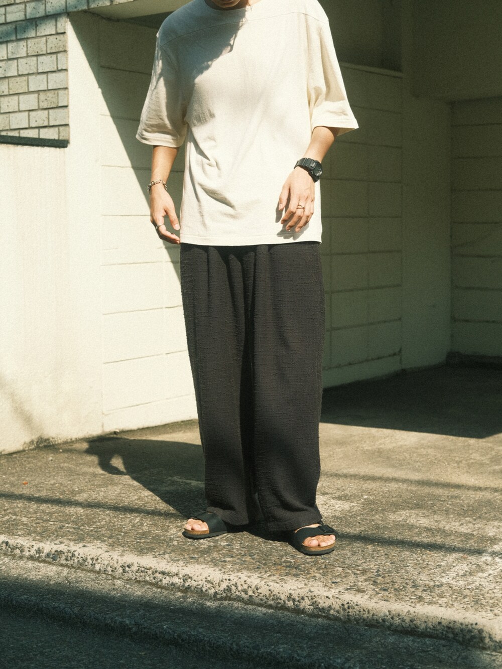 ホワイト系のTシャツ/カットソー、グレー系のその他パンツ、ブラック系のサンダルを着用したメンズの夏コーディネートの3枚目の写真
