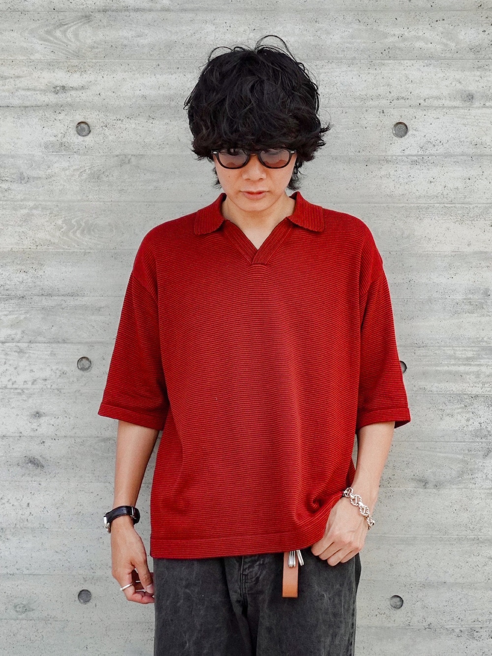 レッド系のポロシャツ、ブラック系のデニムパンツ、ブラック系のサンダルを着用したメンズの夏コーディネートの2枚目の写真