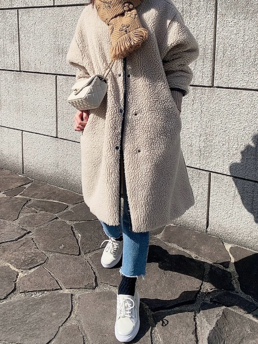 ベージュ系のショルダーバッグ、ベージュ系のノーカラーコート、ブルー系のデニムパンツを着用したレディースの春コーディネートの2枚目の写真