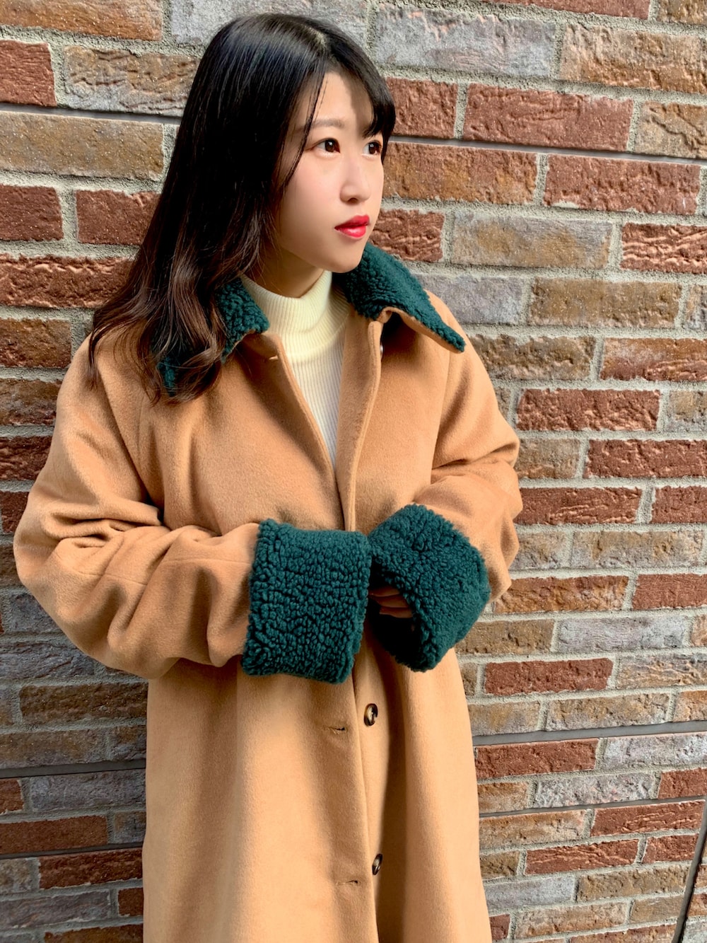 ベージュ系のステンカラーコート、グリーン系のスカート、ホワイト系のニット/セーターを着用したレディースの冬コーディネートの3枚目の写真