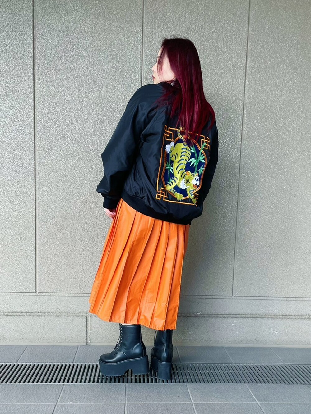 オレンジ系のスカート、ブラック系のブーツ、ブラック系のブルゾンを着用したレディースの冬コーディネートの2枚目の写真