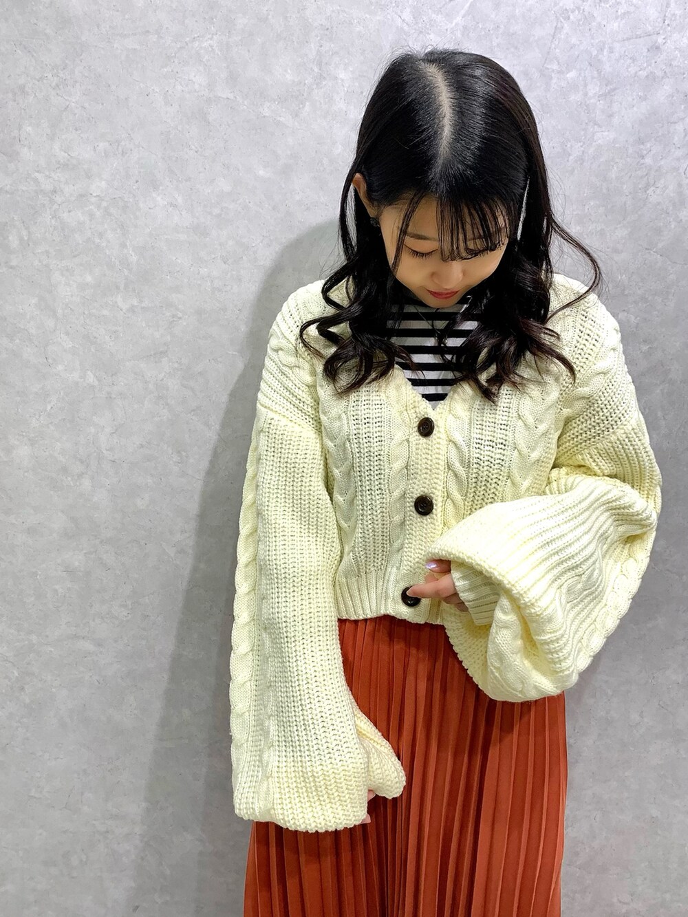 オレンジ系のスカート、ホワイト系のカーディガン/ボレロ、ホワイト系のTシャツ/カットソーを着用したレディースの冬コーディネートの2枚目の写真